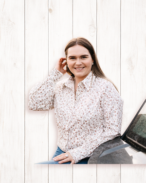 Woman in a floral blouse standing next to a car against a white wooden background