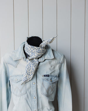 Light blue denim jacket with a floral bandana around the neck against a light gray wooden panel background